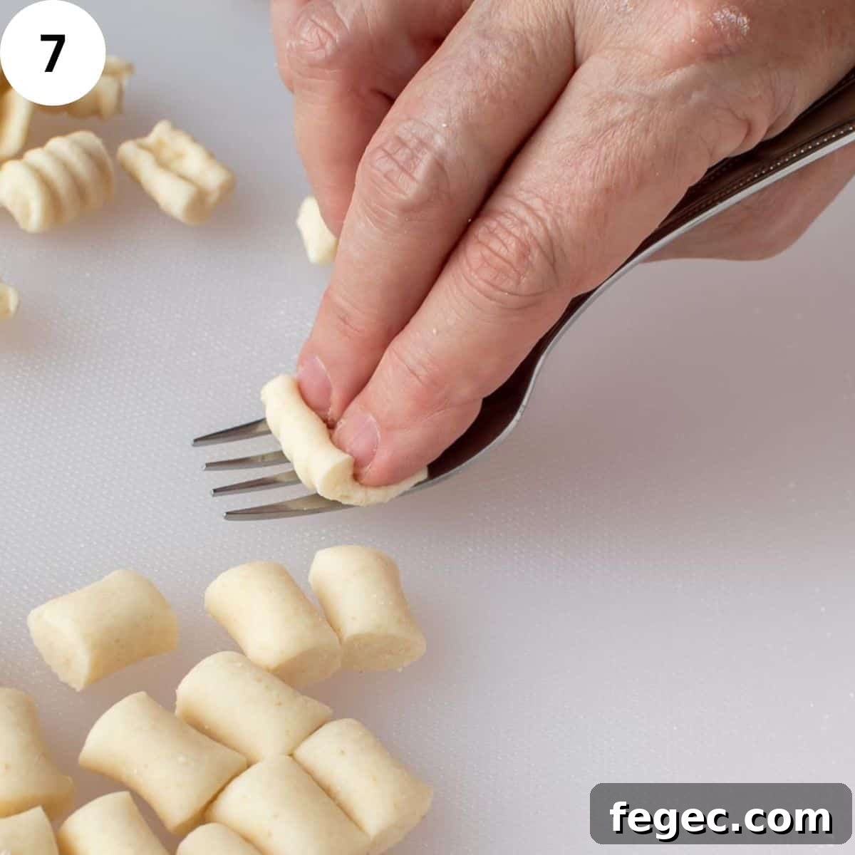 Two fingers using the tynes of a fork to shape pasta dough.