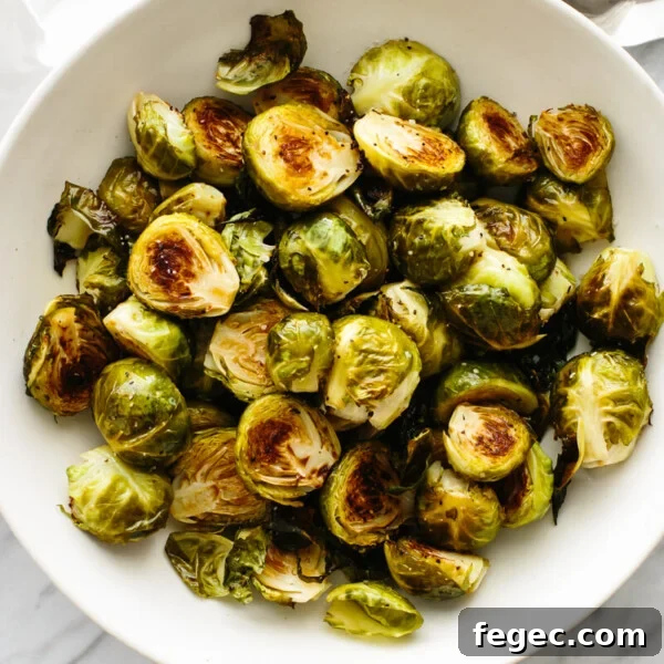 A bowl of roasted Brussels sprouts on a table next to a spoon.