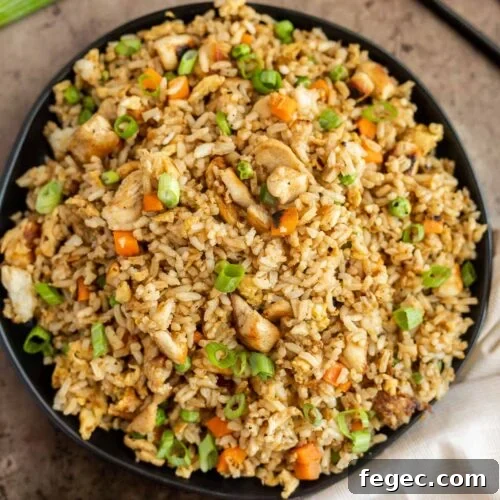 Chicken fried rice with vegetables in a black bowl.