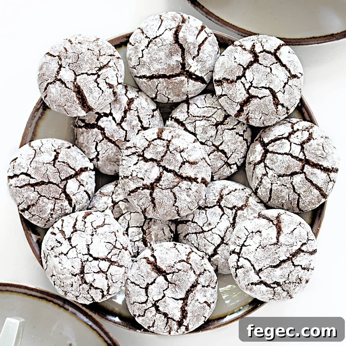 Closeup of cracked tops of powdered sugar covered almond flour chocolate cookies with chocolate cookie dough showing through the cracks.