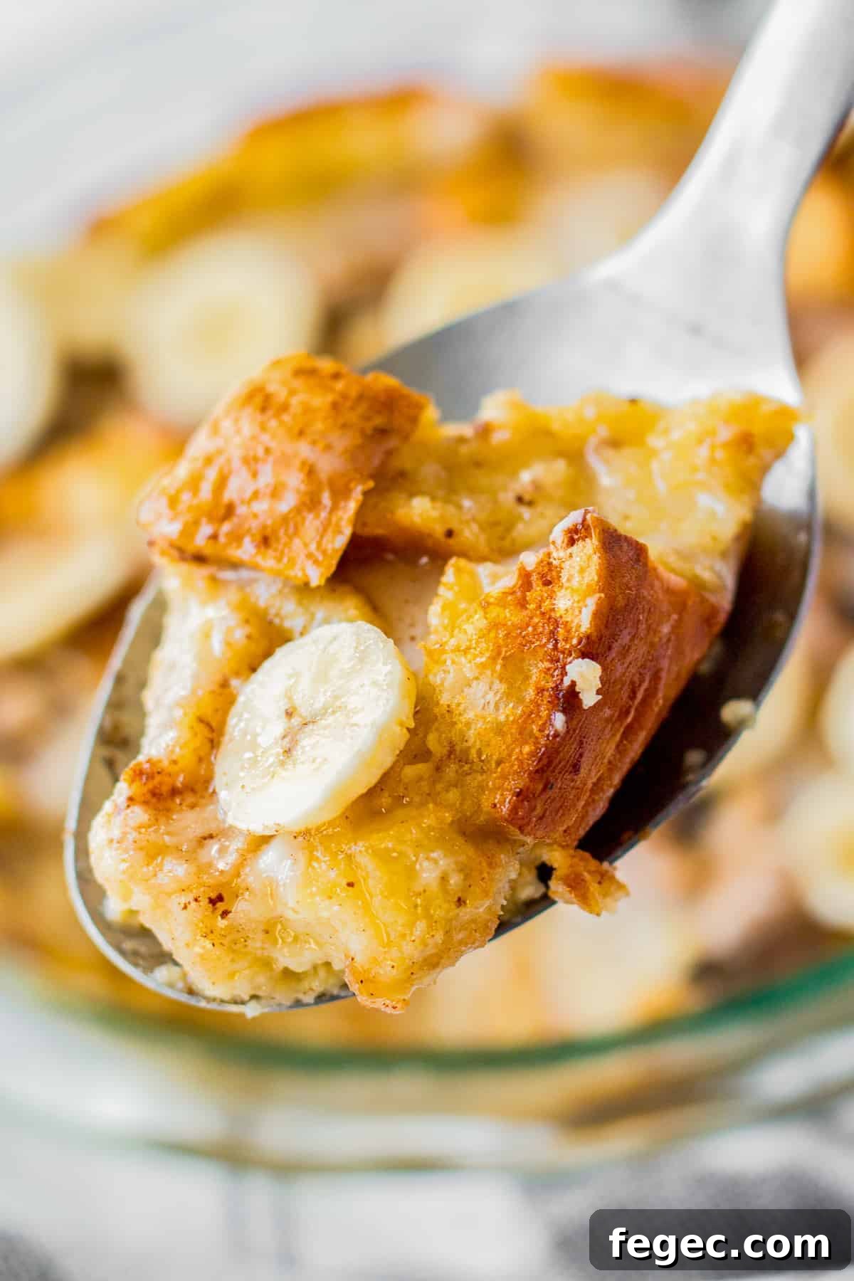 lifting up spoonful of banana bread pudding from a baking dish.