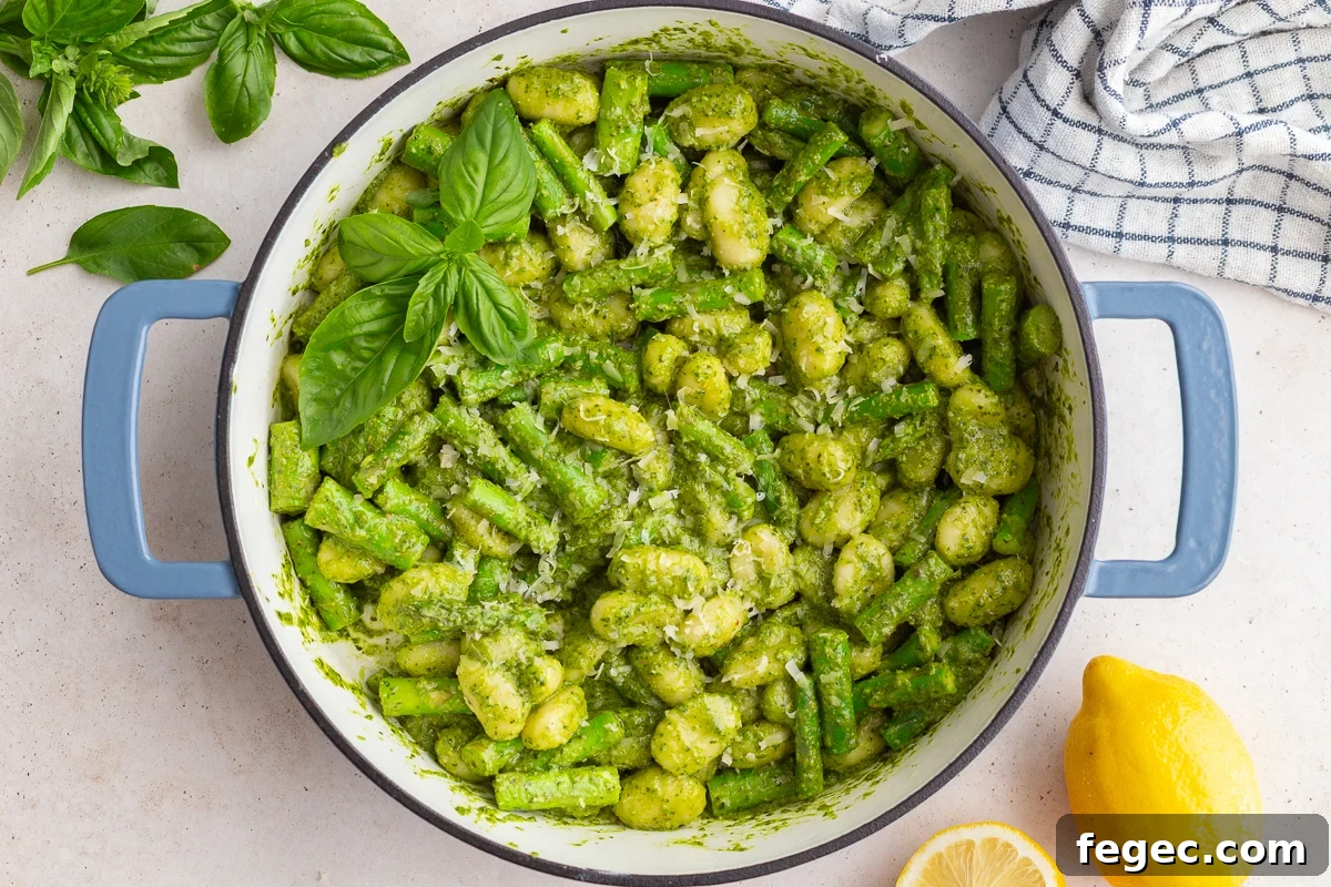 pesto gnocchi in a large skillet with fresh basil and lemon in the corners of the shot