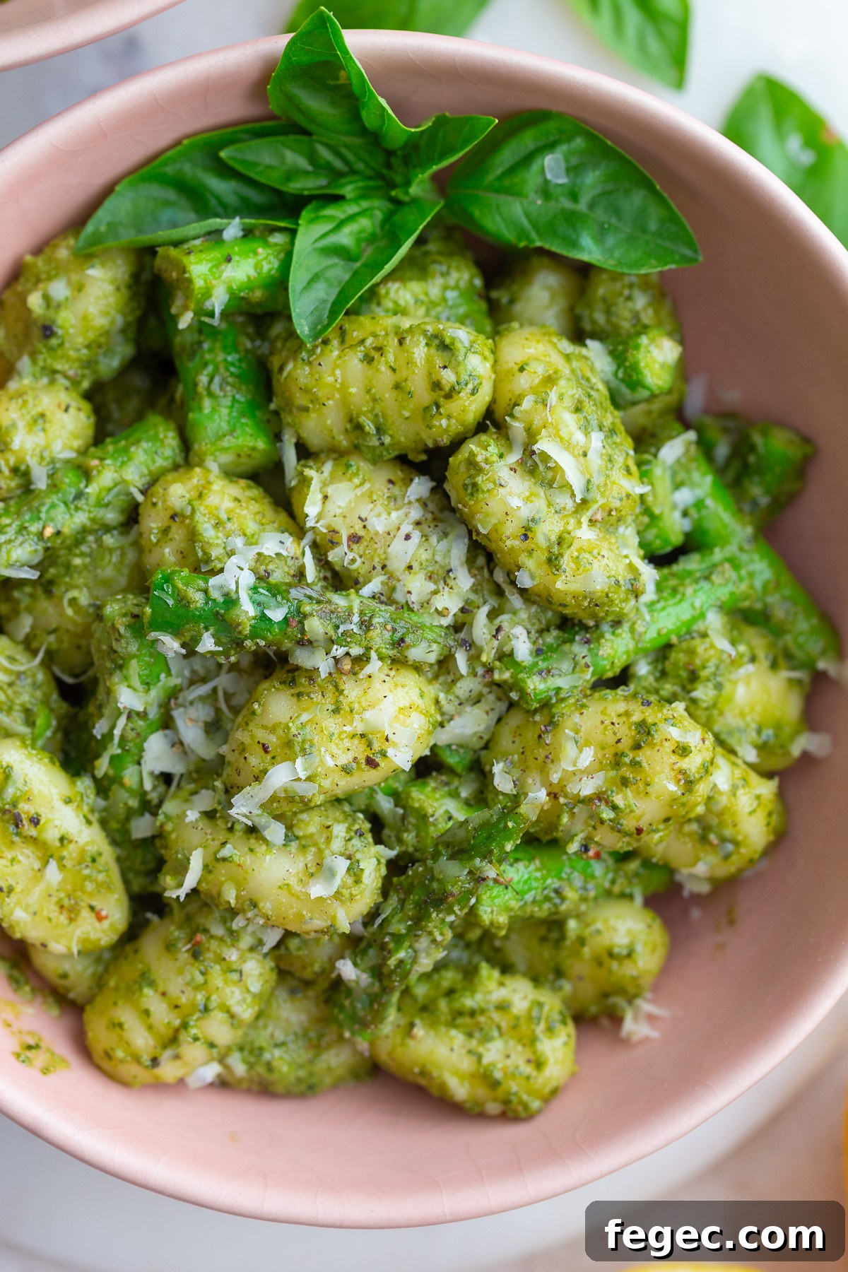 pesto gnocchi in a large bowl with fresh basil and lemon in the corners of the shot