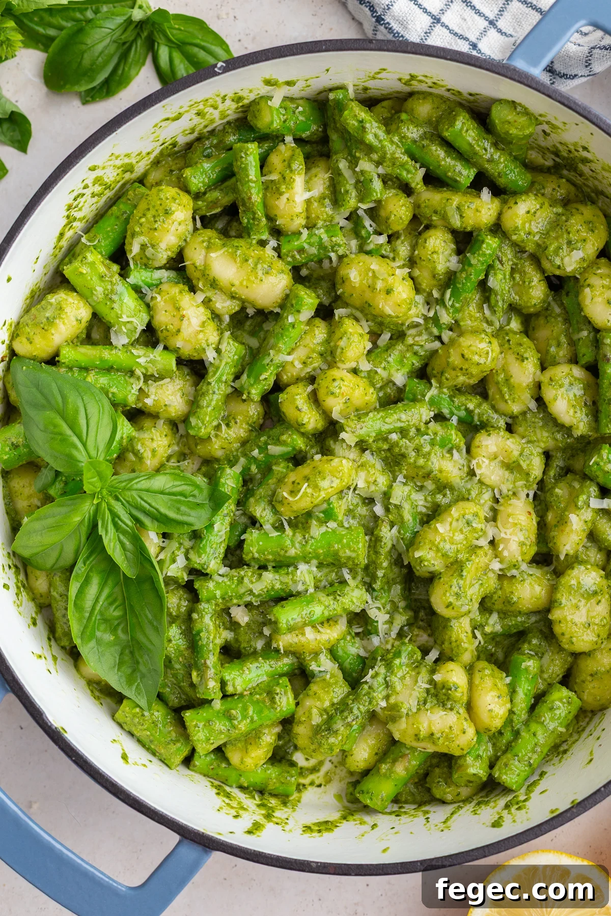 pesto gnocchi in a large skillet with fresh basil and lemon in the corners of the shot
