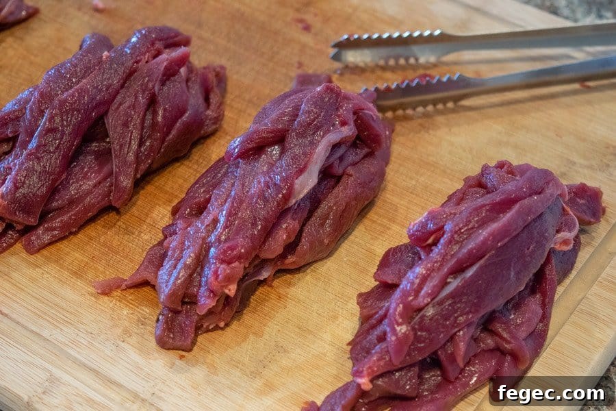 Venison sliced for jerky on cutting board with tongs