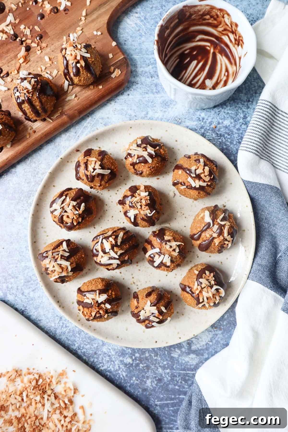 white plate with various biscoff balls topped rolled in crushed biscoff cookies and topped with chocolate drizzle and toasted coconut with chocolate bowl and toasted coconut on a cutting board