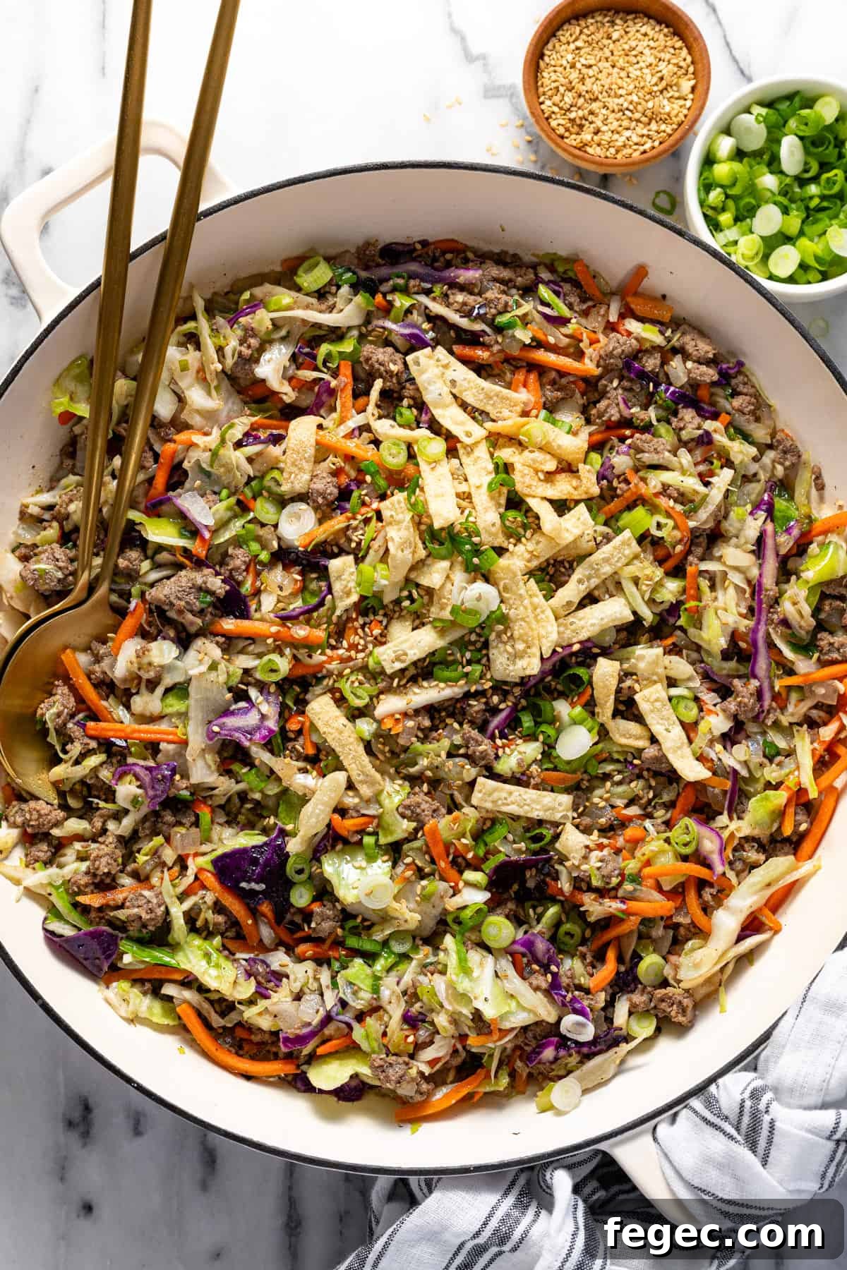 Large white pan filled with homemade egg roll in a bowl mixture garnished with wonton strips, sesame seeds, and green onions.