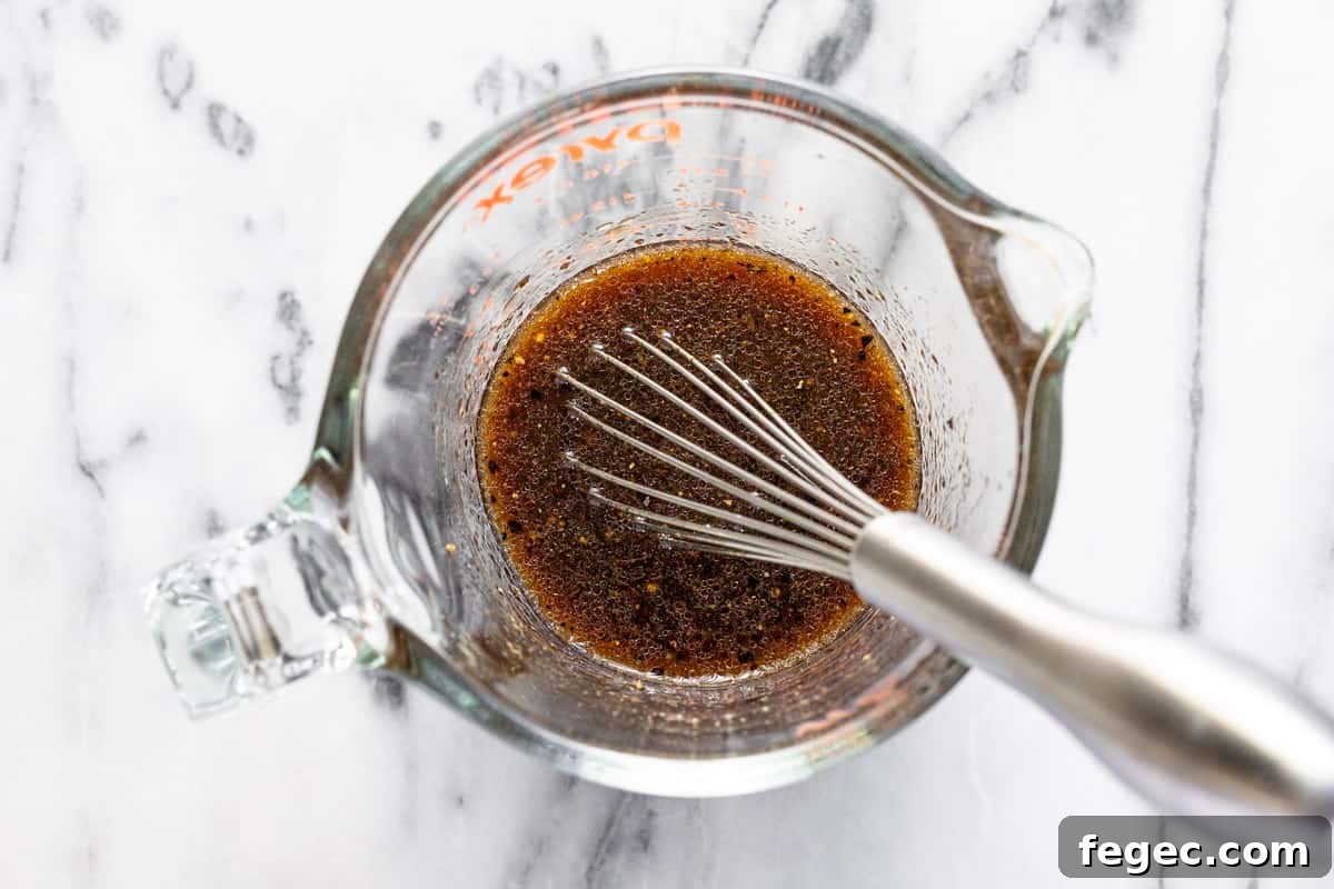 Glass measuring cup filled with egg roll in a bowl sauce.