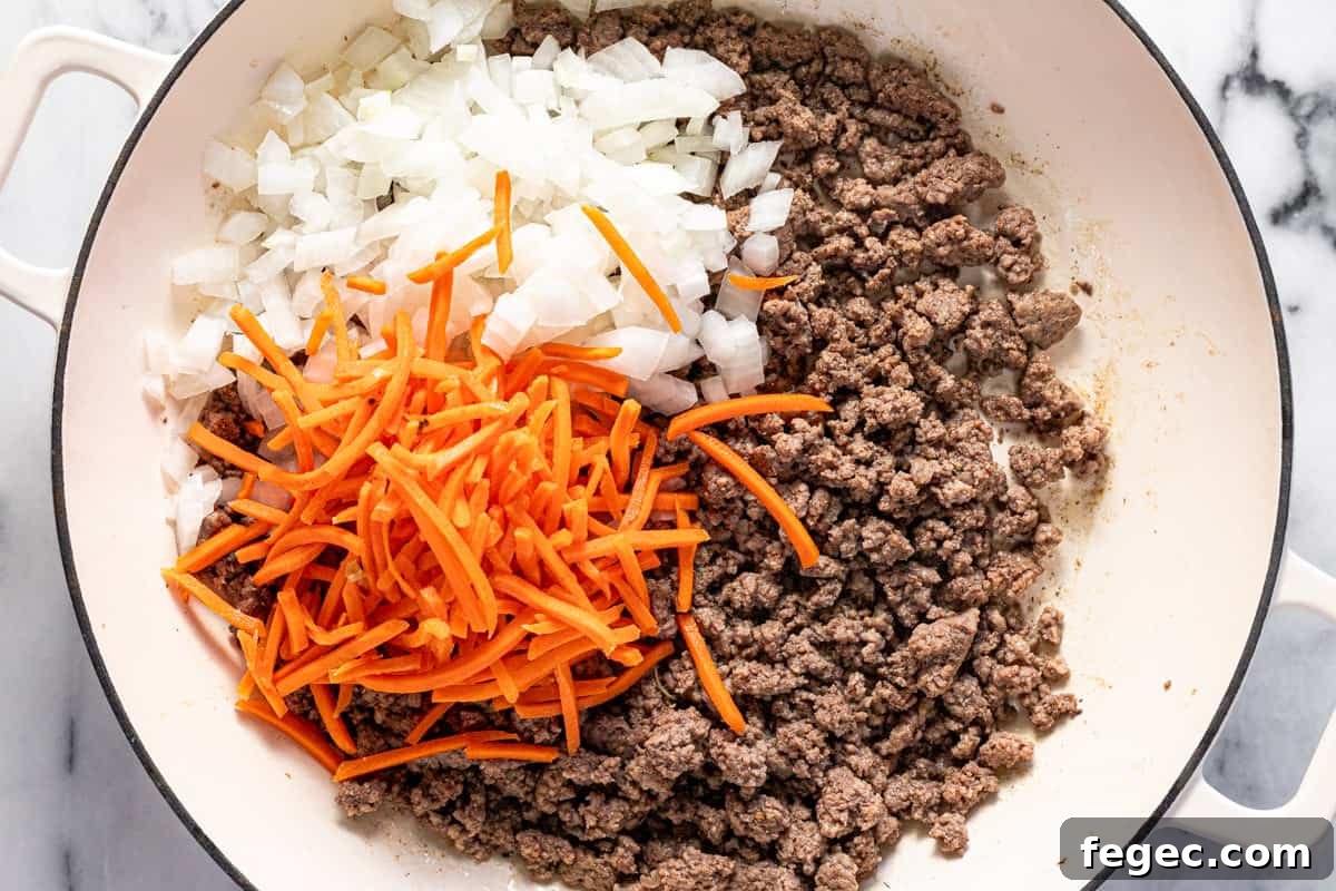 Browned ground beef, diced onion, and matchstick carrots in a large pan.