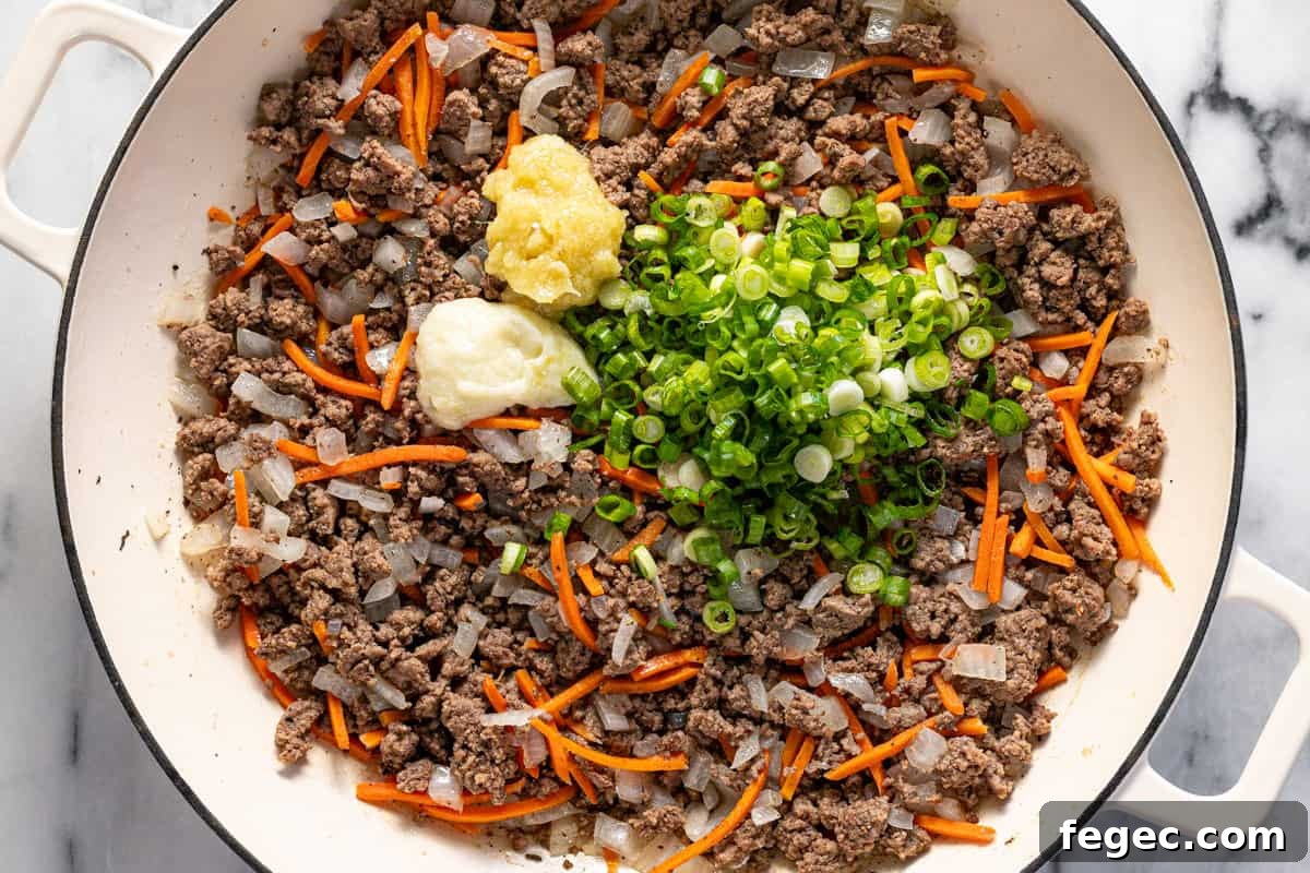 Ground beef with sauteed veggies in a large pan with green onions, garlic paste, and ginger paste.
