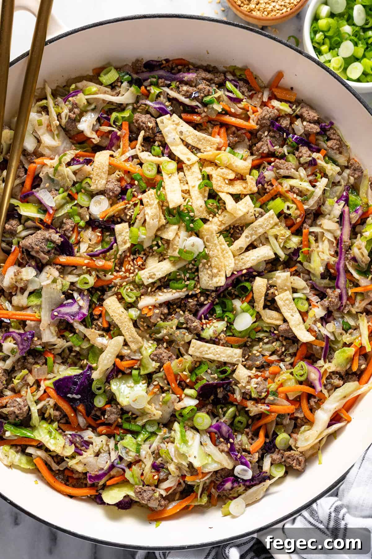 Large white pan filled with homemade egg roll in a bowl mixture garnished with wonton strips, sesame seeds, and green onions.