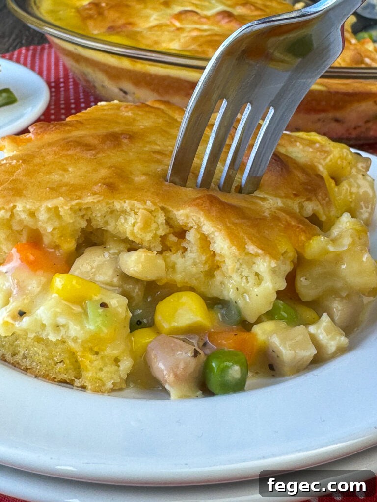 Side view of a piece of chicken pot with corn, peas, carrots and small cubes of chicken baked in a creamy soup mixture and coated with a golden brown layer of Bisquick on top with a fork ready to take a bite.