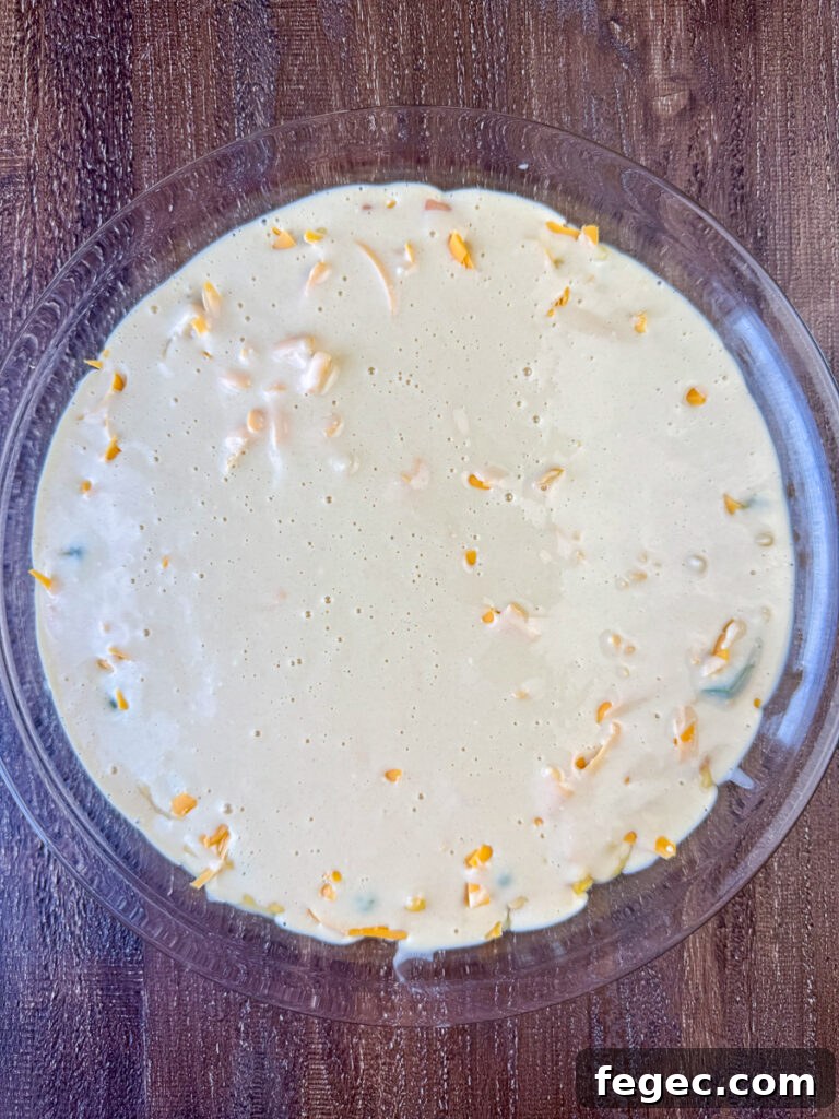 Bisquick baking mix, milk and egg poured over a layer of cheese on a chicken pot pie recipe that's ready to bake.