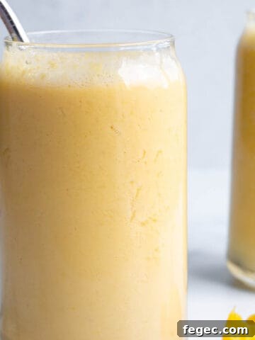 A glass with a yellow smoothie and metal straw.