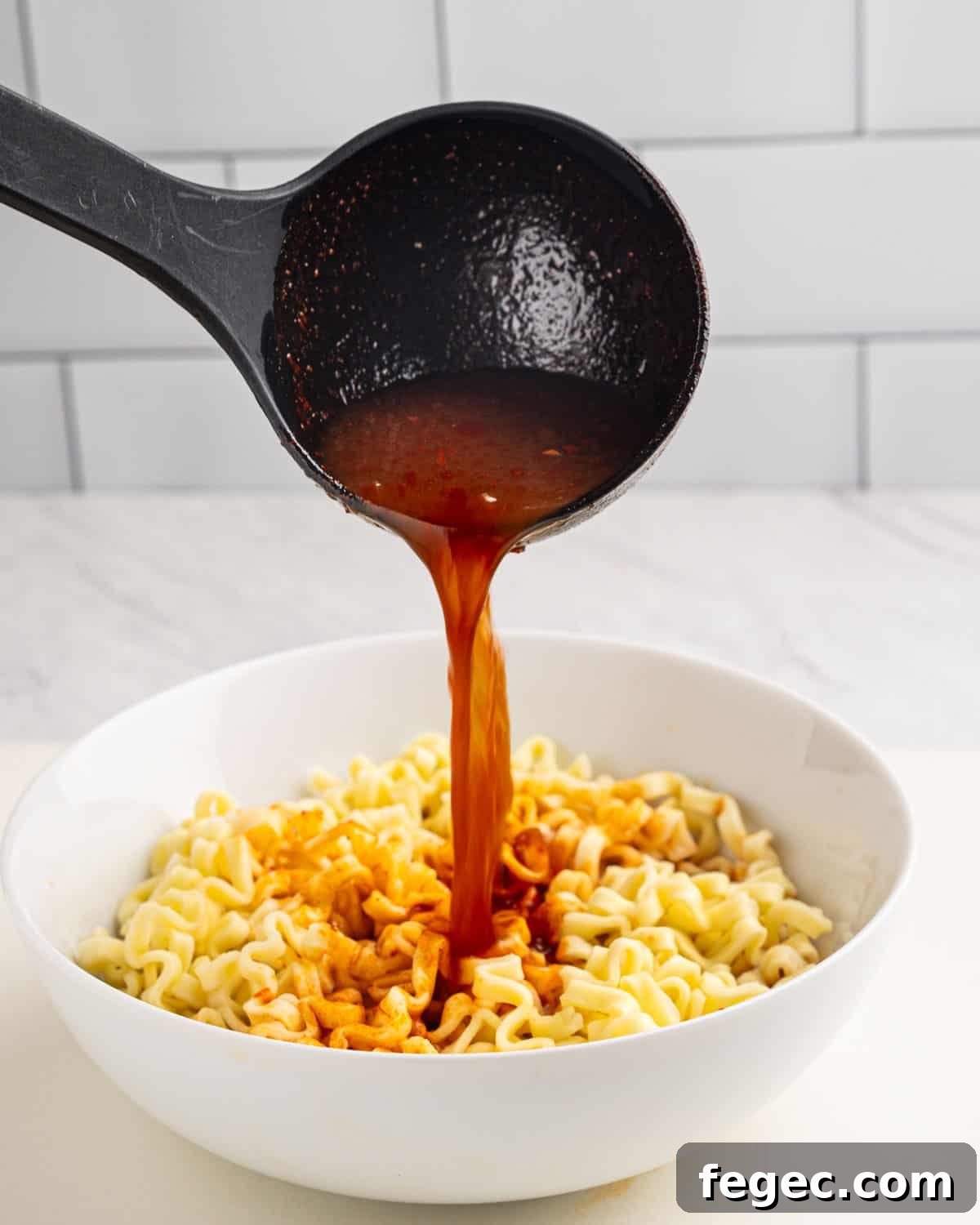 Ladle pouring birria broth onto ramen noodles.